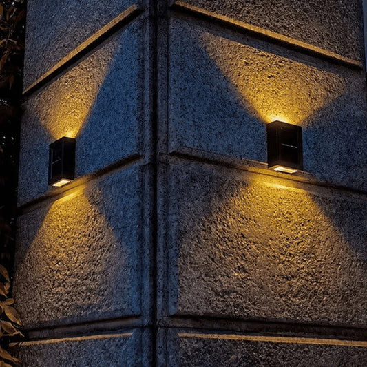SOLARIFY One solar-powered outdoor wall light mounted on a stone wall, projecting warm white light upward and downward. IP65 weatherproof. Suitable for garden fences, façades, covered terraces and entrance walls.