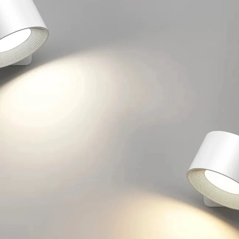 LUNIFY 360 wireless rechargeable LED spotlight with a circular concentric ring surround, mounted on a wall and casting warm amber light in a minimal interior — equally suited as a freestanding spotlight on a shelf or side table.