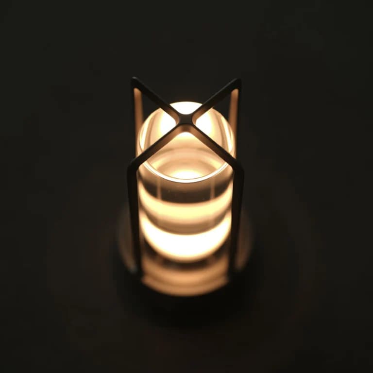 AMBIENTIFY Retro cordless retro table lantern lamp casting a warm amber glow, placed on a wooden tray. Slender aluminium frame with cylindrical acrylic glass shade. Atmospheric home décor lighting for bedroom, living room or outdoor use.