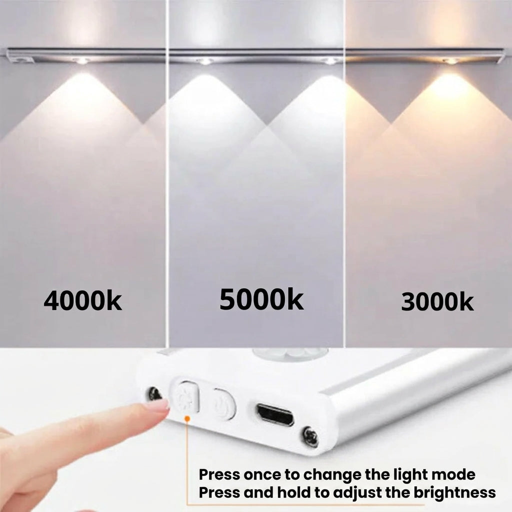 AMBIENTIFY Sora slim rechargeable LED light bar mounted beneath a wooden shelf above a home desk, casting warm even light across the workspace — motion sensor under-cabinet lighting in brushed aluminium.