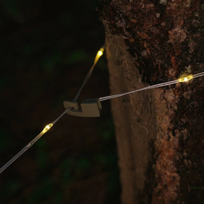 Campify String fairy light reel held in hand at night, showing warm amber LED string lights extended across dark outdoor ground, compact hub glowing with blue charge indicator, IP67 waterproof camping and home fairy lights.