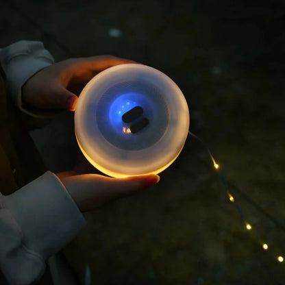 Campify String fairy light reel held in hand at night, showing warm amber LED string lights extended across dark outdoor ground, compact hub glowing with blue charge indicator, IP67 waterproof camping and home fairy lights.