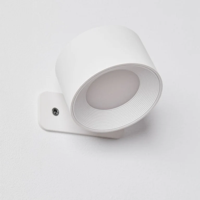 LUNIFY 360 wireless rechargeable LED spotlight with a circular concentric ring surround, mounted on a wall and casting warm amber light in a minimal interior — equally suited as a freestanding spotlight on a shelf or side table.