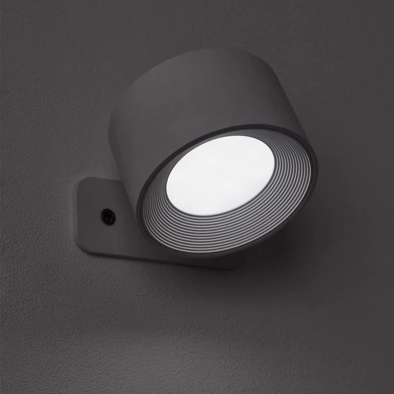 LUNIFY 360 wireless rechargeable LED spotlight with a circular concentric ring surround, mounted on a wall and casting warm amber light in a minimal interior — equally suited as a freestanding spotlight on a shelf or side table.