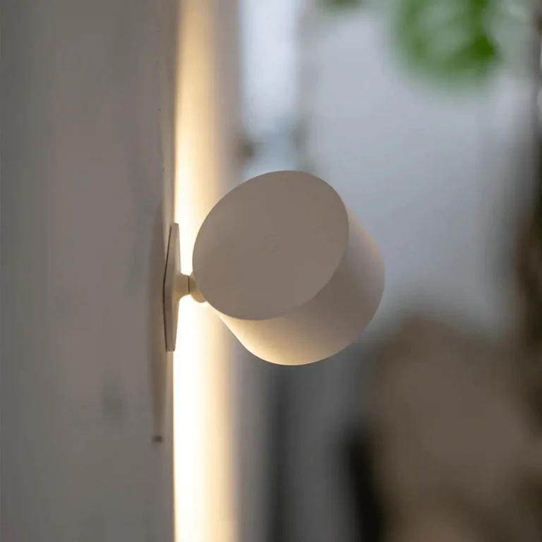 LUNIFY 360 wireless rechargeable LED spotlight with a circular concentric ring surround, mounted on a wall and casting warm amber light in a minimal interior — equally suited as a freestanding spotlight on a shelf or side table.