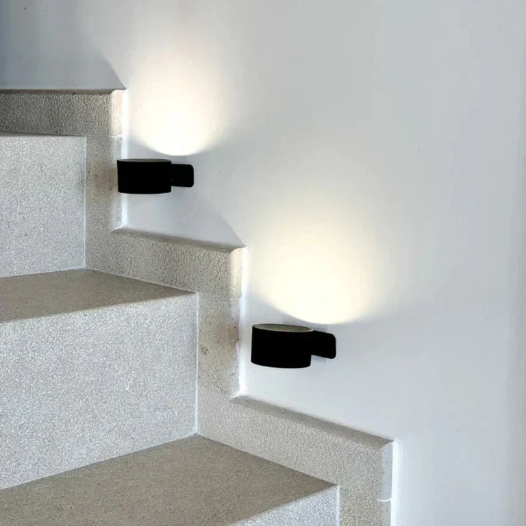 LUNIFY 360 wireless rechargeable LED spotlight with a circular concentric ring surround, mounted on a wall and casting warm amber light in a minimal interior — equally suited as a freestanding spotlight on a shelf or side table.