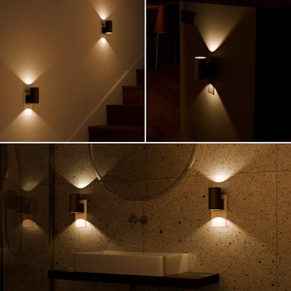 PLUGIFY One plug-in wall light in matte finish mounted in a bedroom wall socket, casting warm ambient light onto a wooden bedside table with a remote control and ceramic mug beside it.