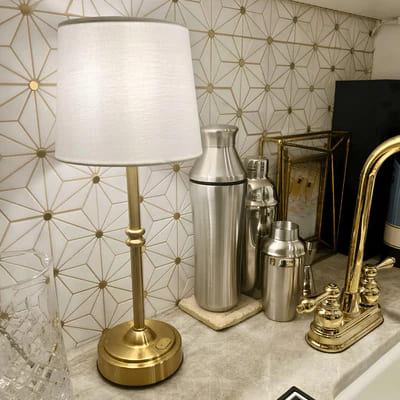 AMBIENTIFY Classic cordless table lamp with fabric shade and iron stem, casting warm ambient light on a bedside table. Three brightness settings and up to 40 hours battery life. Suitable for bedroom, living room and home office.