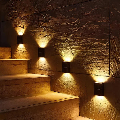 SOLARIFY One solar-powered outdoor wall light mounted on a stone wall, projecting warm white light upward and downward. IP65 weatherproof. Suitable for garden fences, façades, covered terraces and entrance walls.