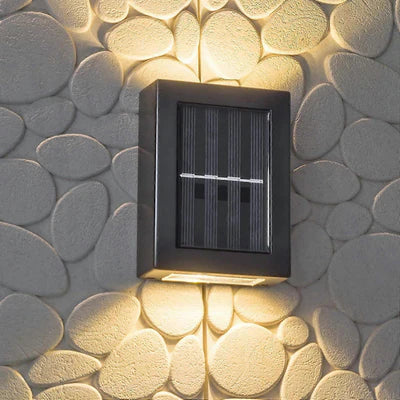 SOLARIFY One solar-powered outdoor wall light mounted on a stone wall, projecting warm white light upward and downward. IP65 weatherproof. Suitable for garden fences, façades, covered terraces and entrance walls.