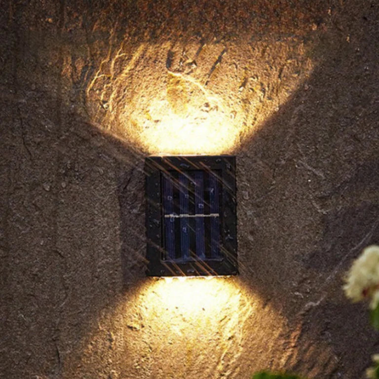 SOLARIFY One solar-powered outdoor wall light mounted on a stone wall, projecting warm white light upward and downward. IP65 weatherproof. Suitable for garden fences, façades, covered terraces and entrance walls.